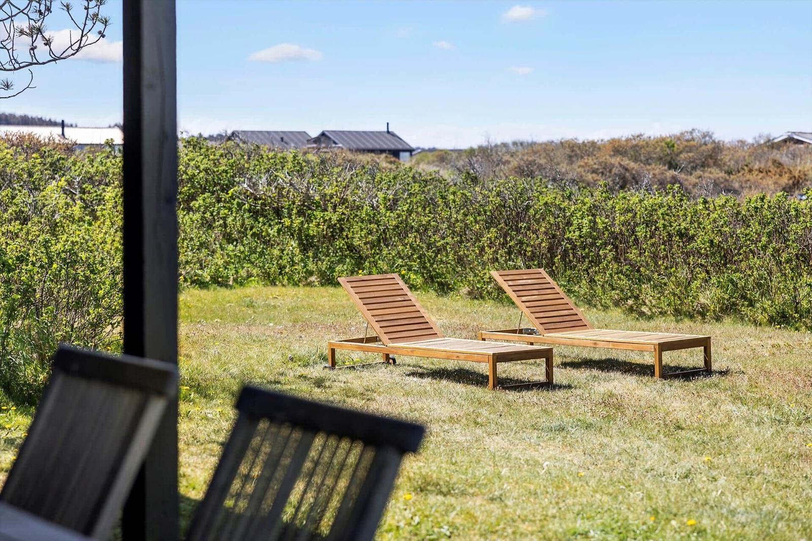 Two wooden lounge chairs on a lawn with view of shrubs and houses.