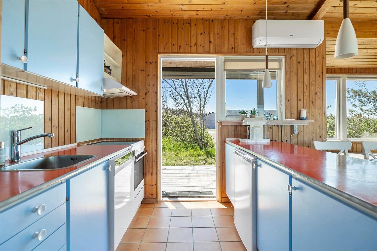 Kitchen with blue cabinets, red countertop, and wooden walls. Passage to terrace with view of greenery.