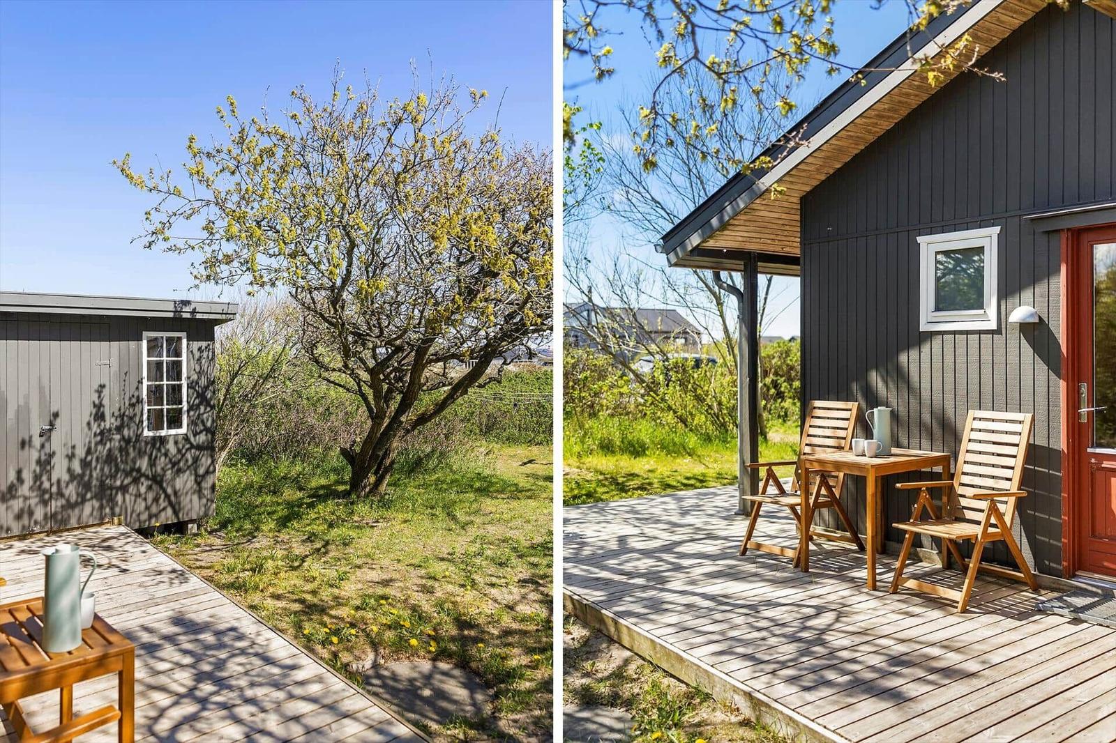 Wooden terrace with table and chairs in front of gray house. Tree with yellow blossoms in background.