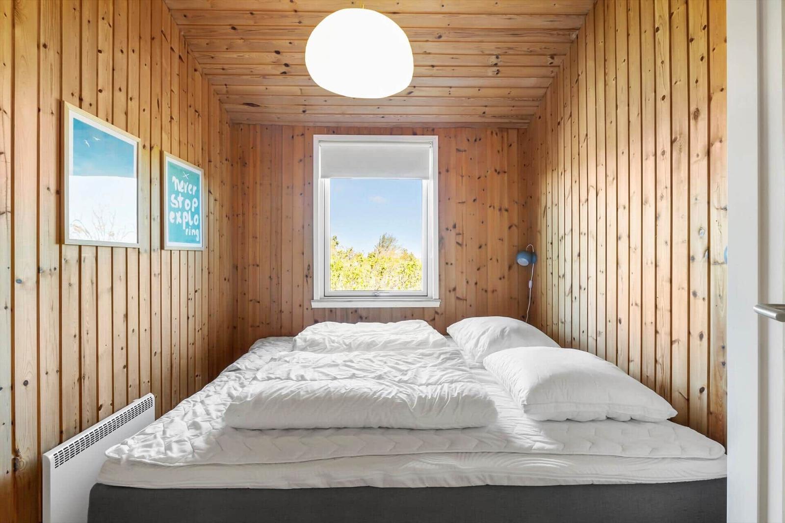 Bedroom with wooden walls, bed, and window. Ceiling light and wall art.