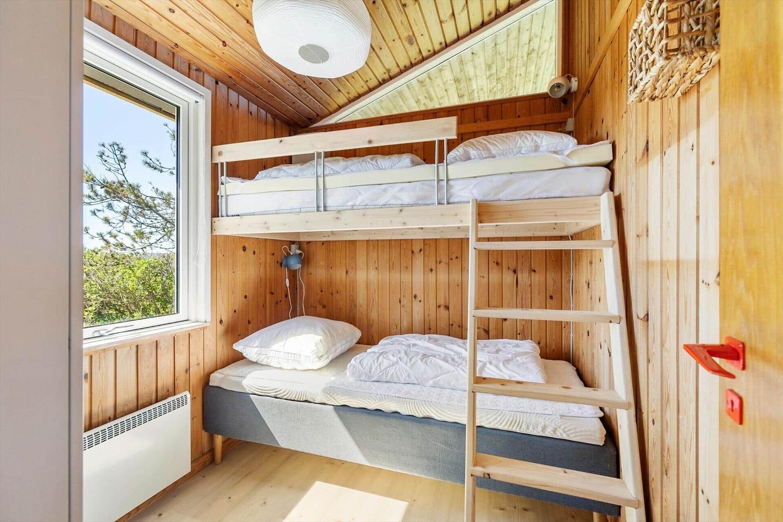 Bedroom with bunk bed, wooden walls, and window with view of trees.