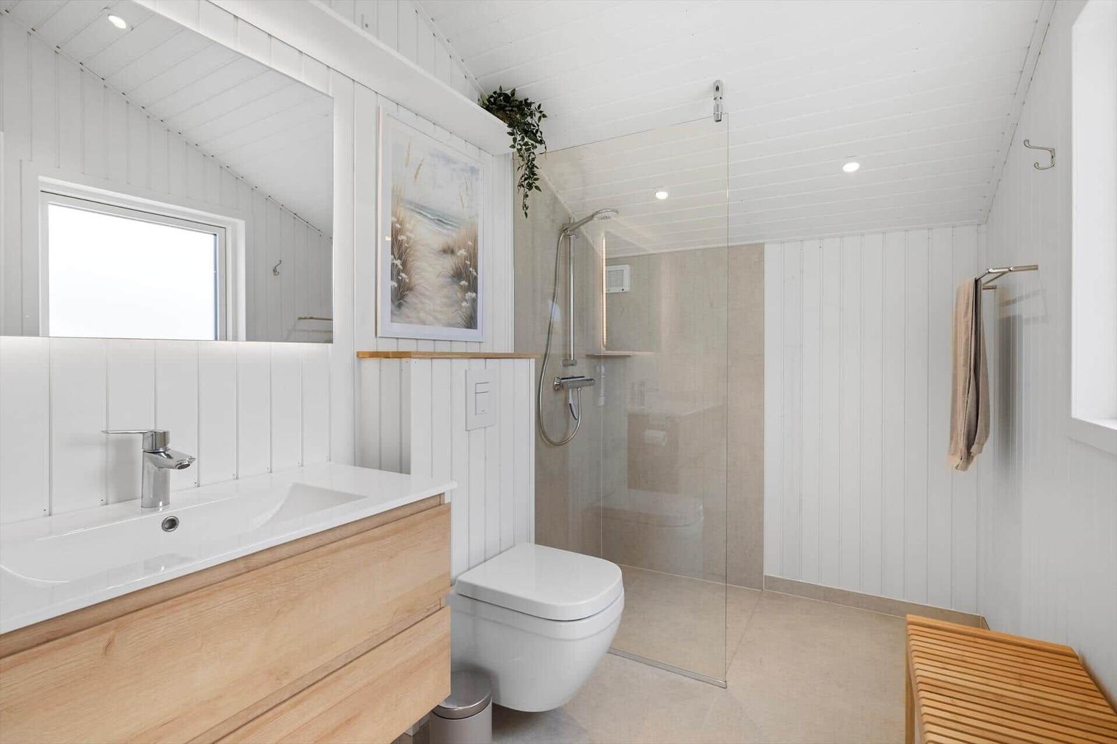 Badezimmer mit Dusche, Waschbecken und Toilette. Weiße Wände und Holzelemente.
