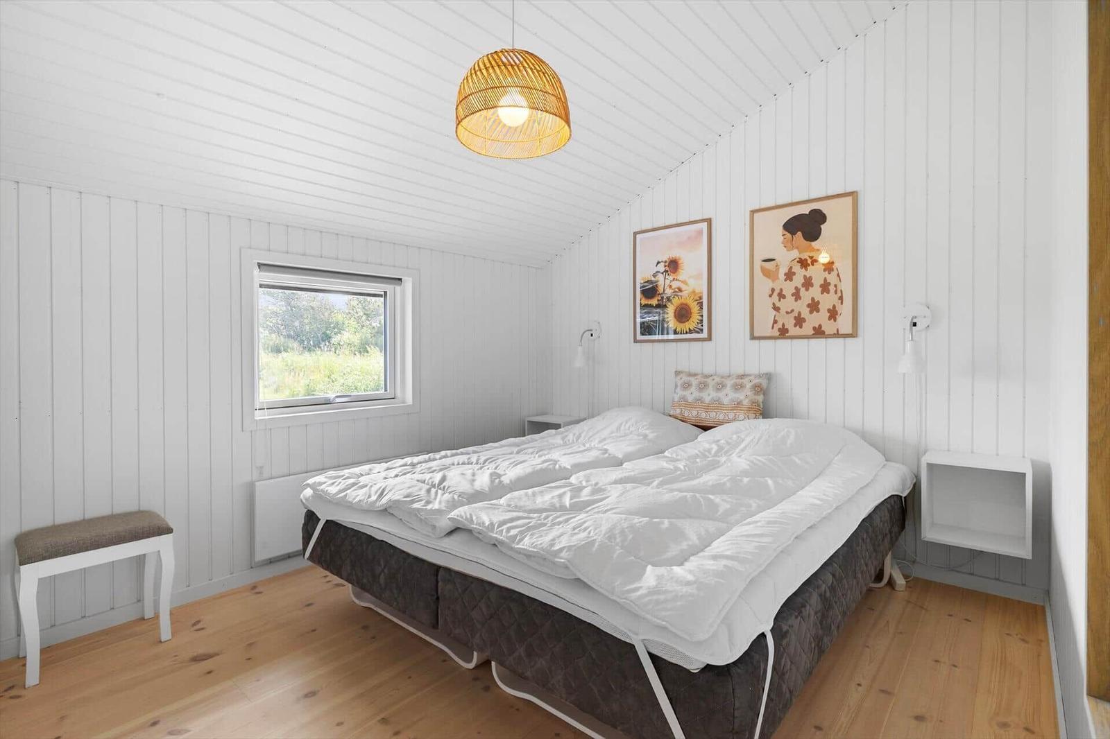 Schlafzimmer mit Bett, Fenster und Wandbildern.