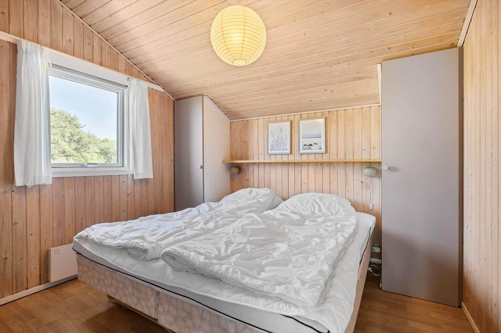 Schlafzimmer mit Holzwand, Bett und Fenster. Decke mit Lampen.