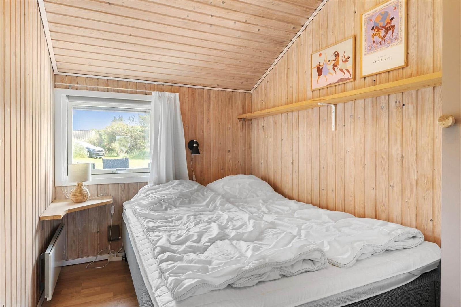 Schlafzimmer mit Holzwand, Bett und Fenster mit Blick nach draußen.