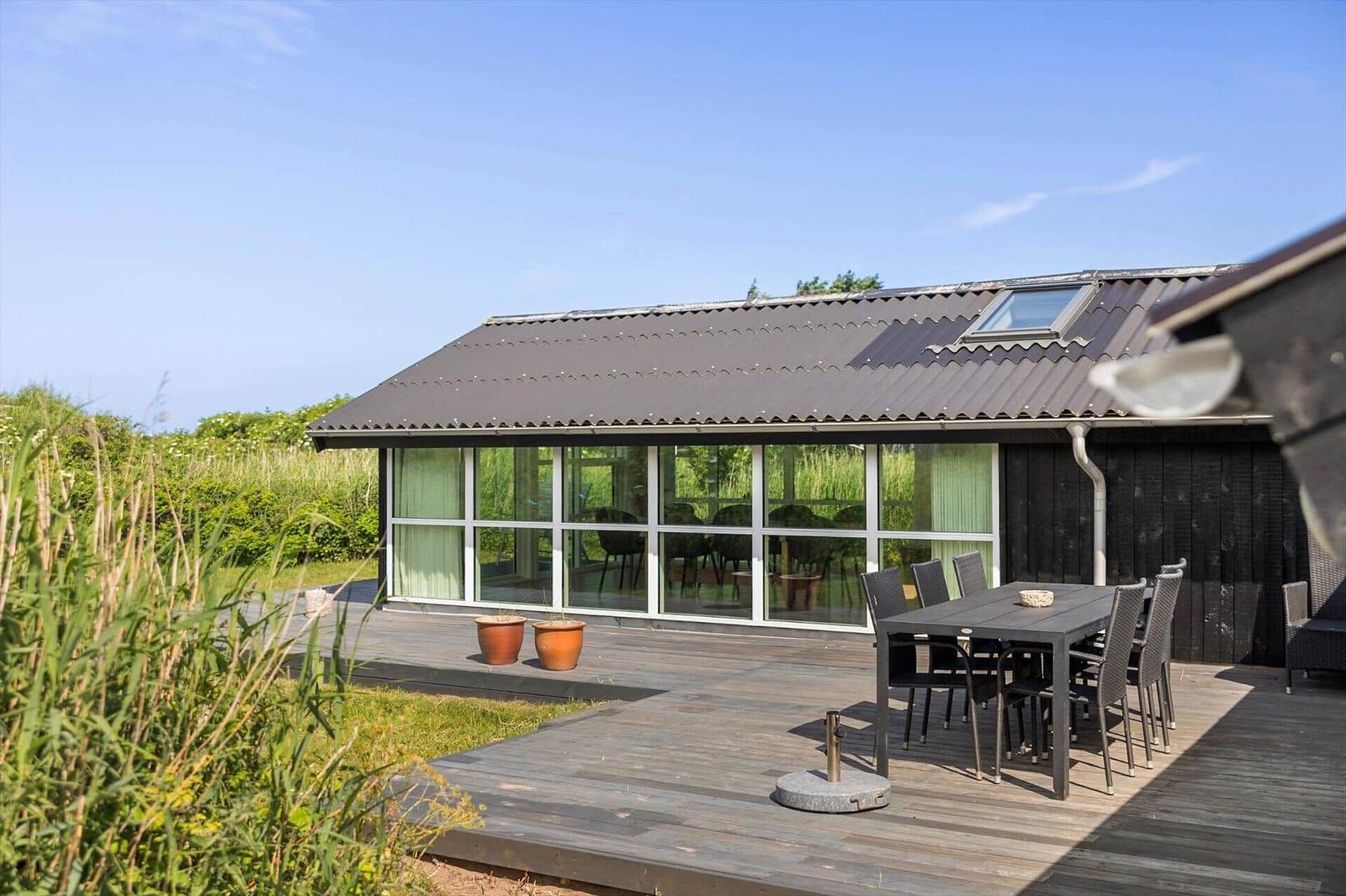 Moderne Villa mit großem Holzterrasse, Gartenmöbel und großflächigen Fenstern.