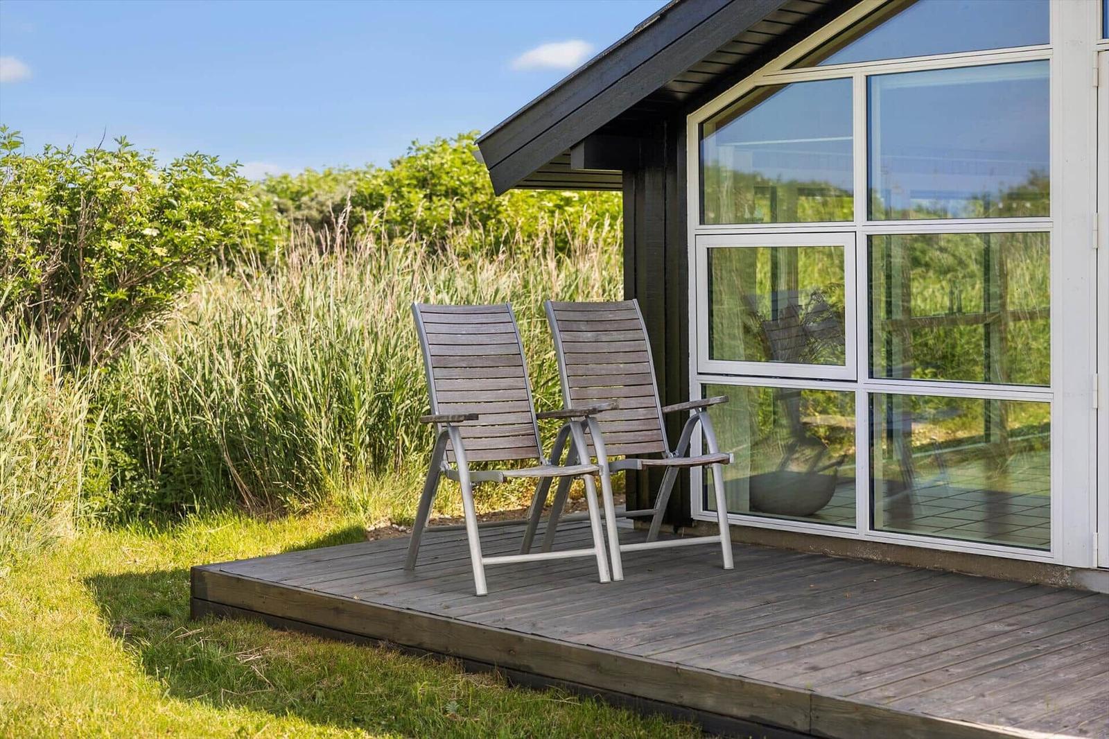 Terrasse mit zwei Liegestühlen vor einem Haus mit großem Fenster.