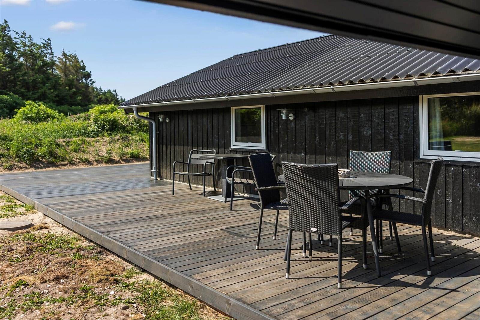 Terrasse mit Tisch und Stühlen vor einem Holzhaus mit schwarzem Dach.