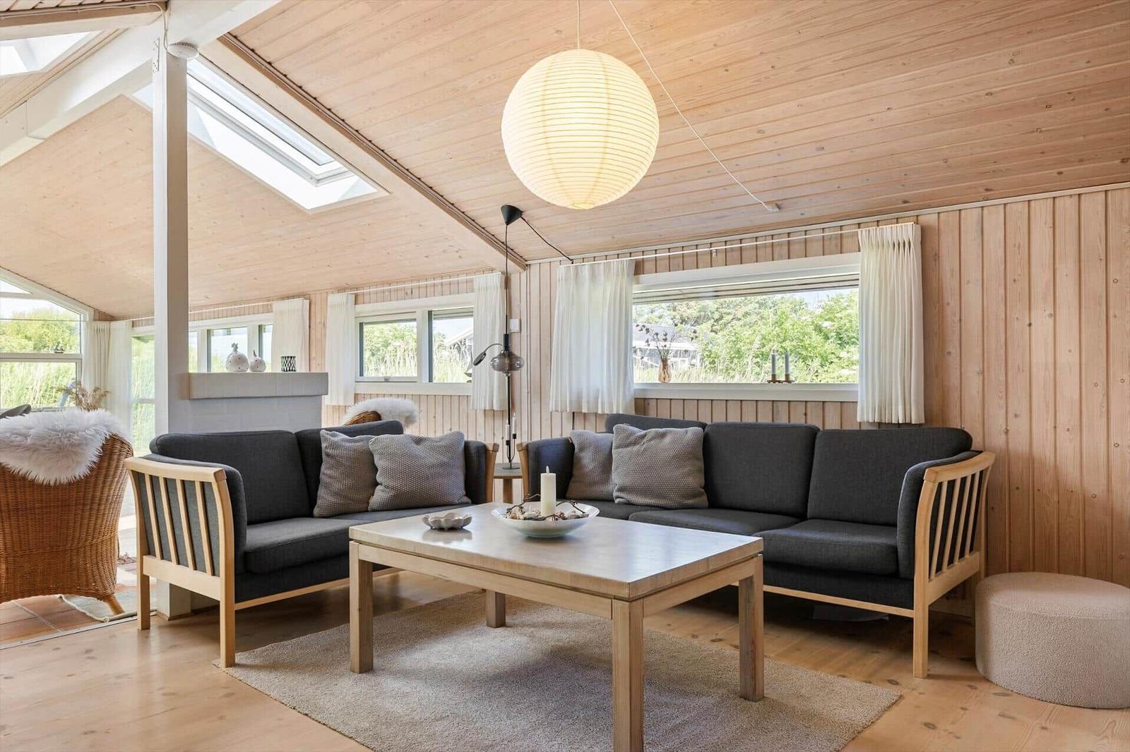 Wohnzimmer mit Holzwand, Sofa, Tisch und Lampe. Fenster und Dachfenster.