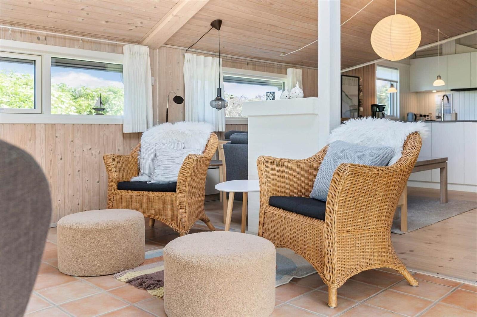 Zwei geflochtene Sessel mit Felldecken und Kissen stehen vor Fenstern mit Holzwand.