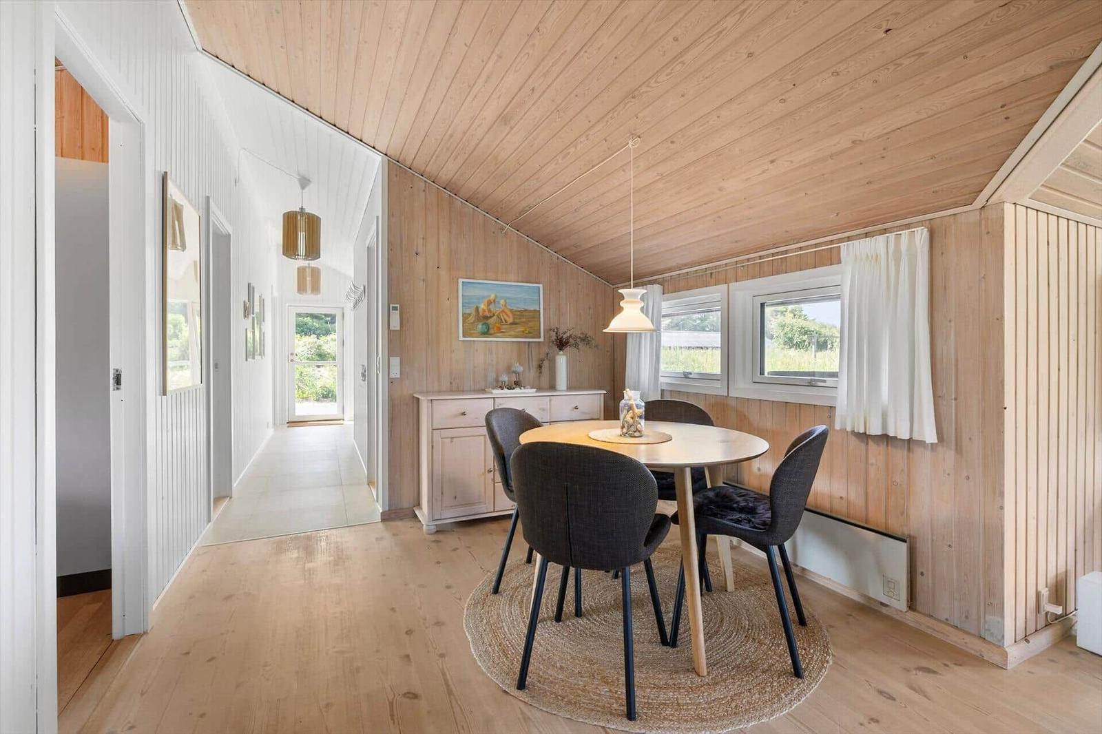 Essbereich mit runden Tisch und vier Stühlen. Holzwände und -decke. Fenster mit weißen Vorhängen.