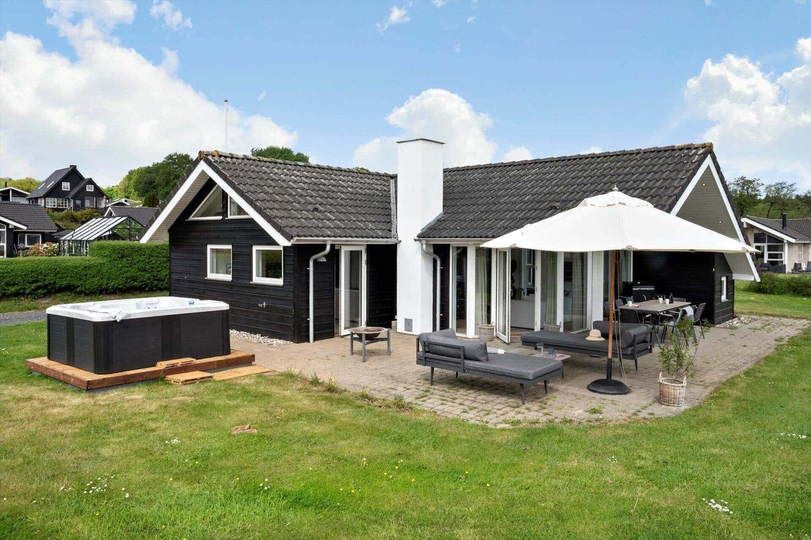 Modern holiday home with outdoor terrace, sun umbrella, seating, and hot tub in garden.