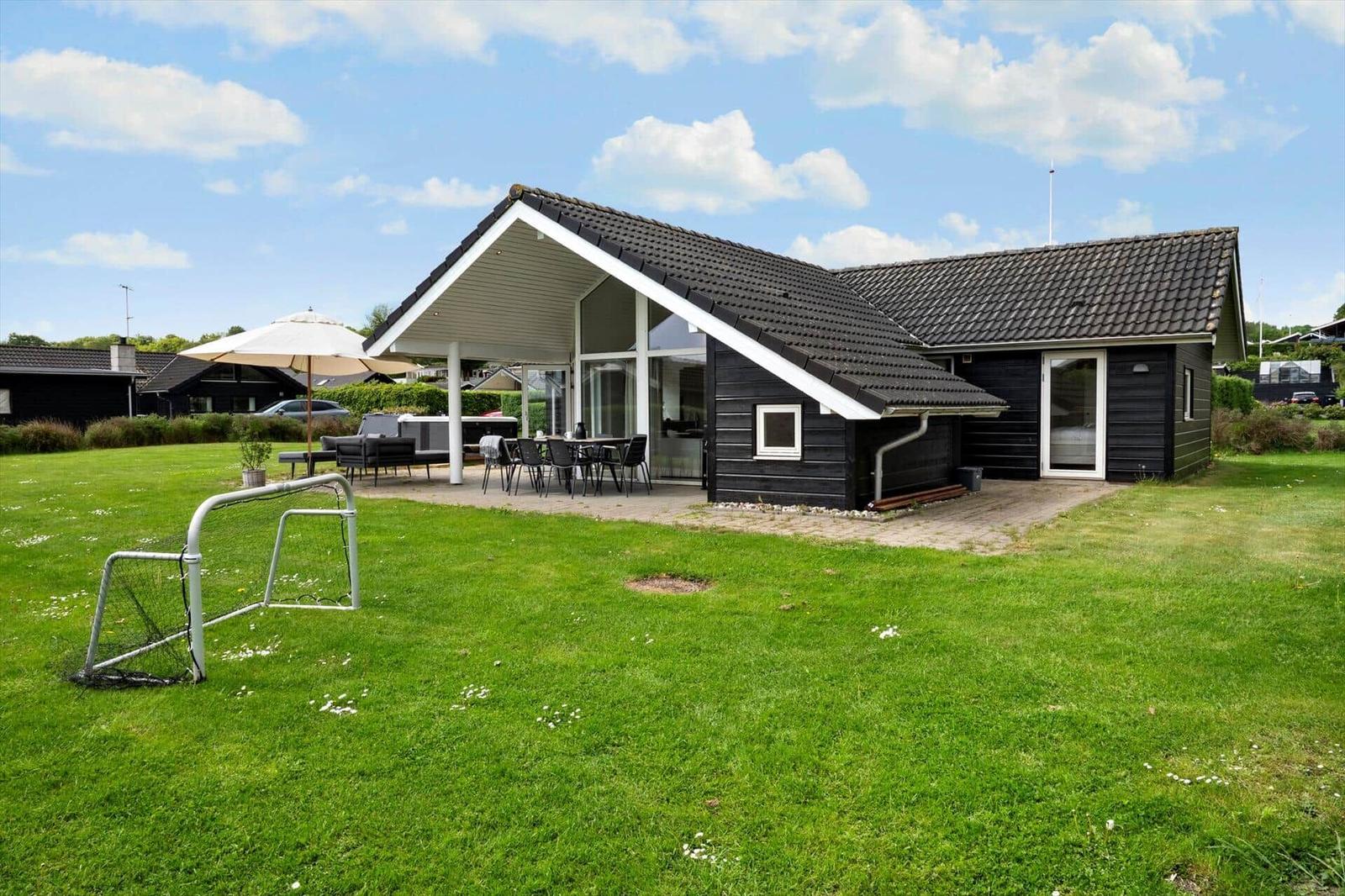 Black wooden house with terrace and garden. Outdoor table, seating group, and soccer goal.