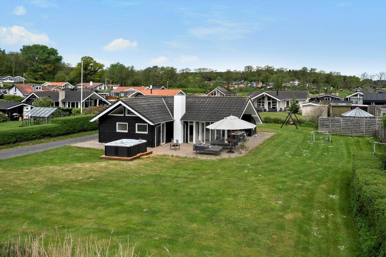 Modern villa with large garden, hot tub, and terrace. View of residential houses in the background.