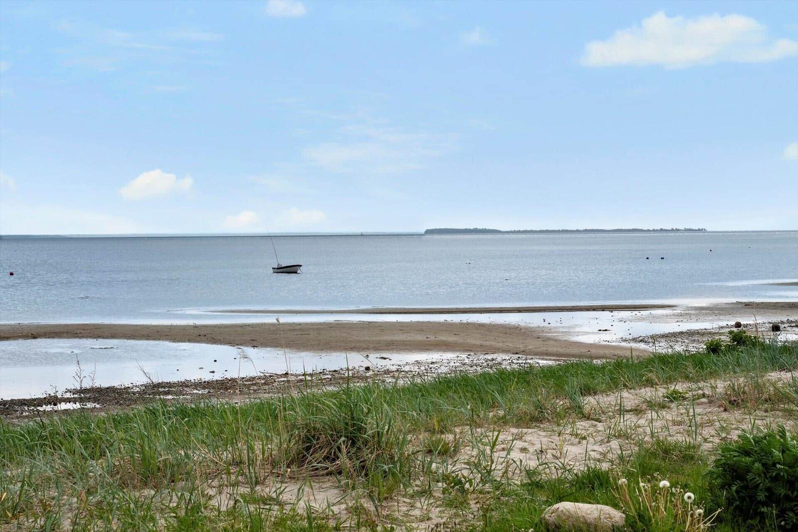 A small boat is on the water. Grass and sand are visible in the foreground.