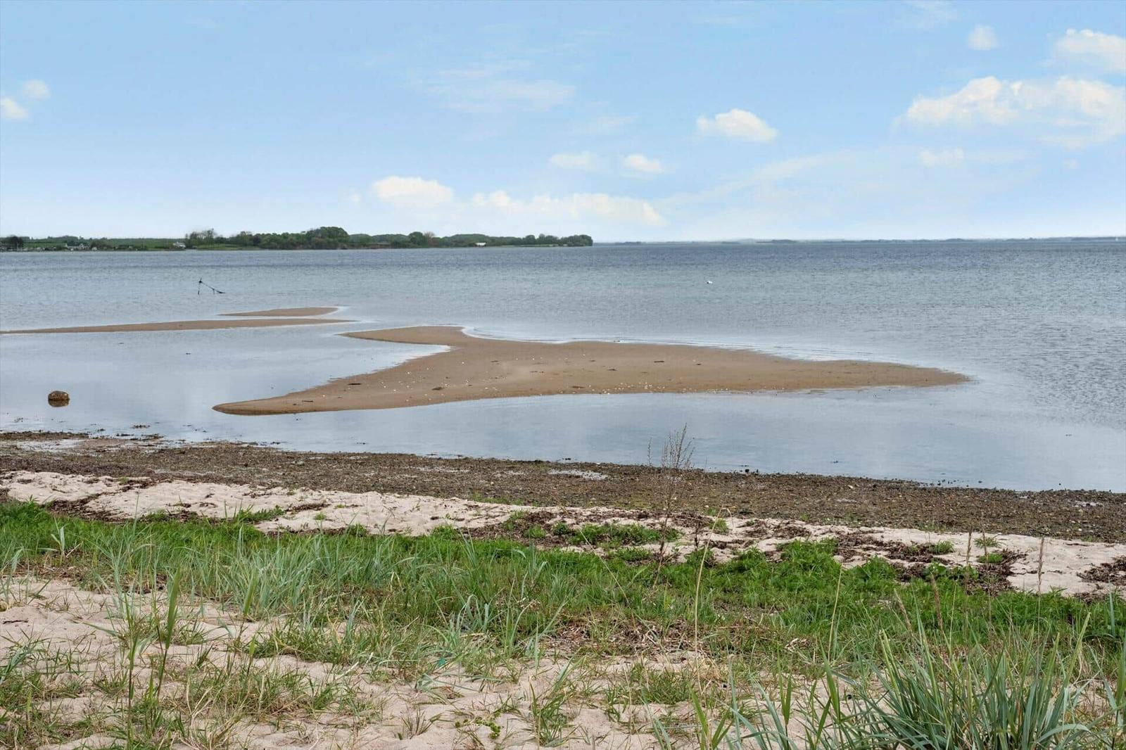 Sandy beach with shallow water and distant greenery under a clear sky.