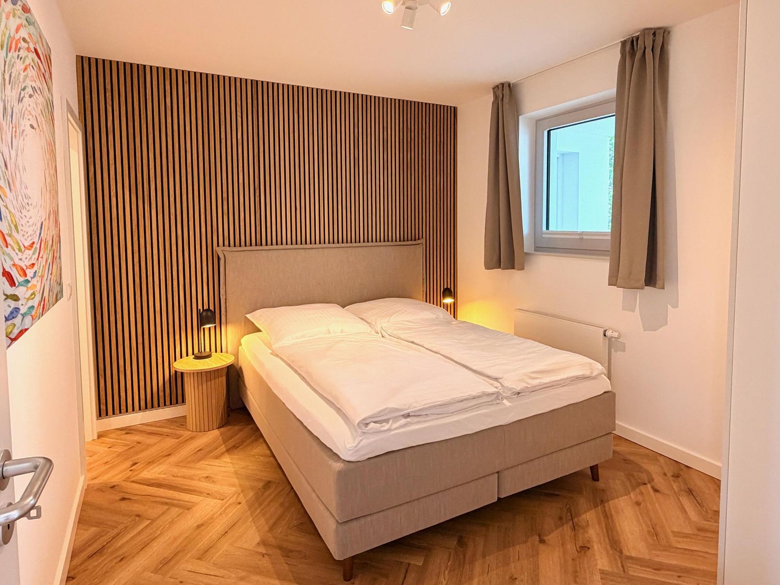 Schlafzimmer mit Bett, Holzwand und Fenster. Holzfußboden und Nachttisch.