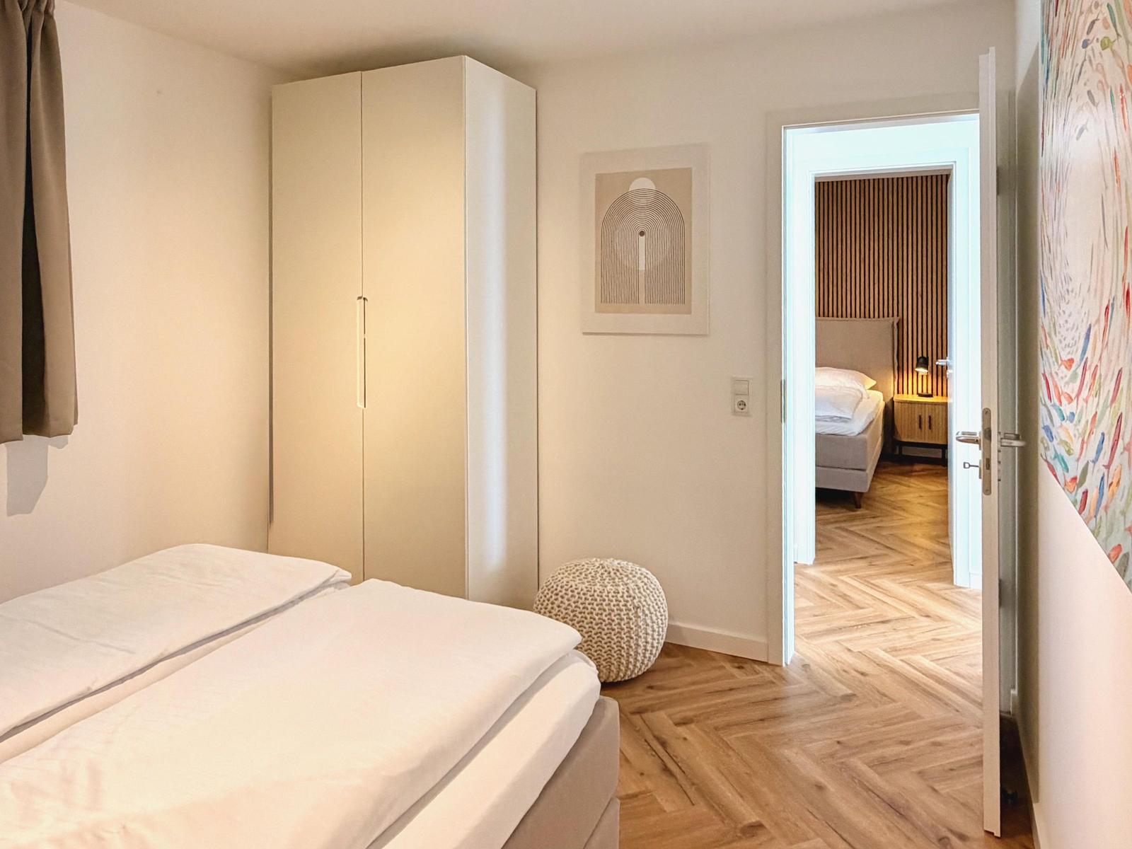 Schlafzimmer mit Bett, Kleiderschrank und Tür zum Anschlussraum mit Holzboden.