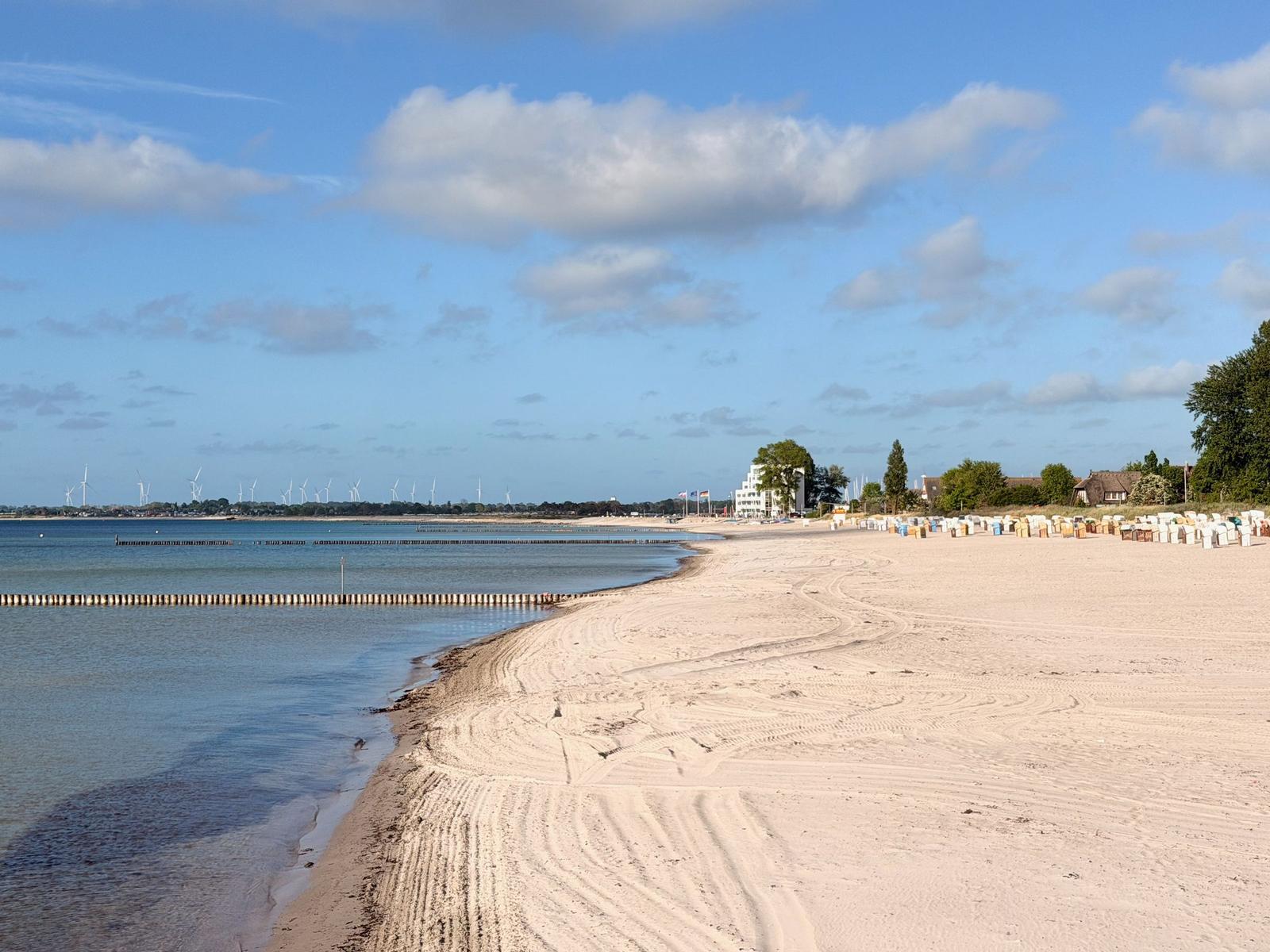 Strand mit Sand, Watt und Strandkörben unter blauem Himmel mit Wolken.