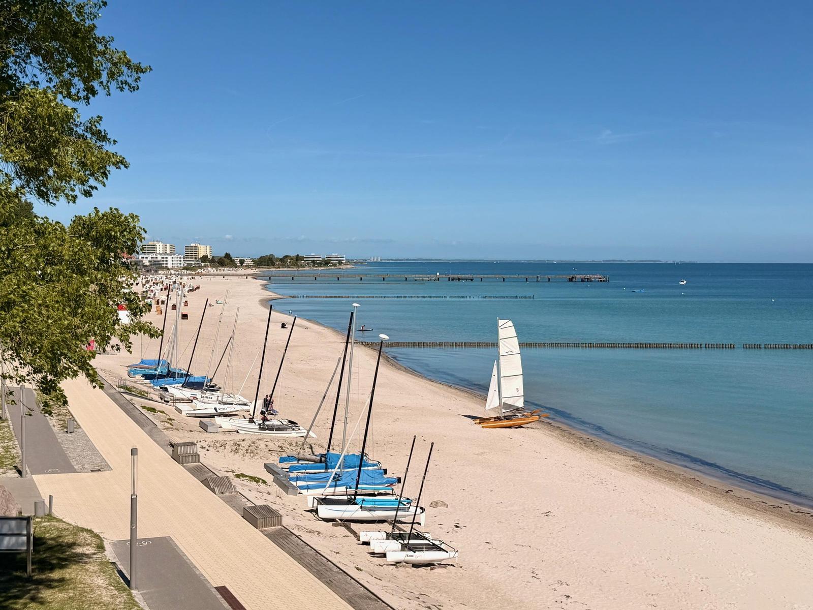 Strand mit Segelbooten und Promenade unter blauem Himmel