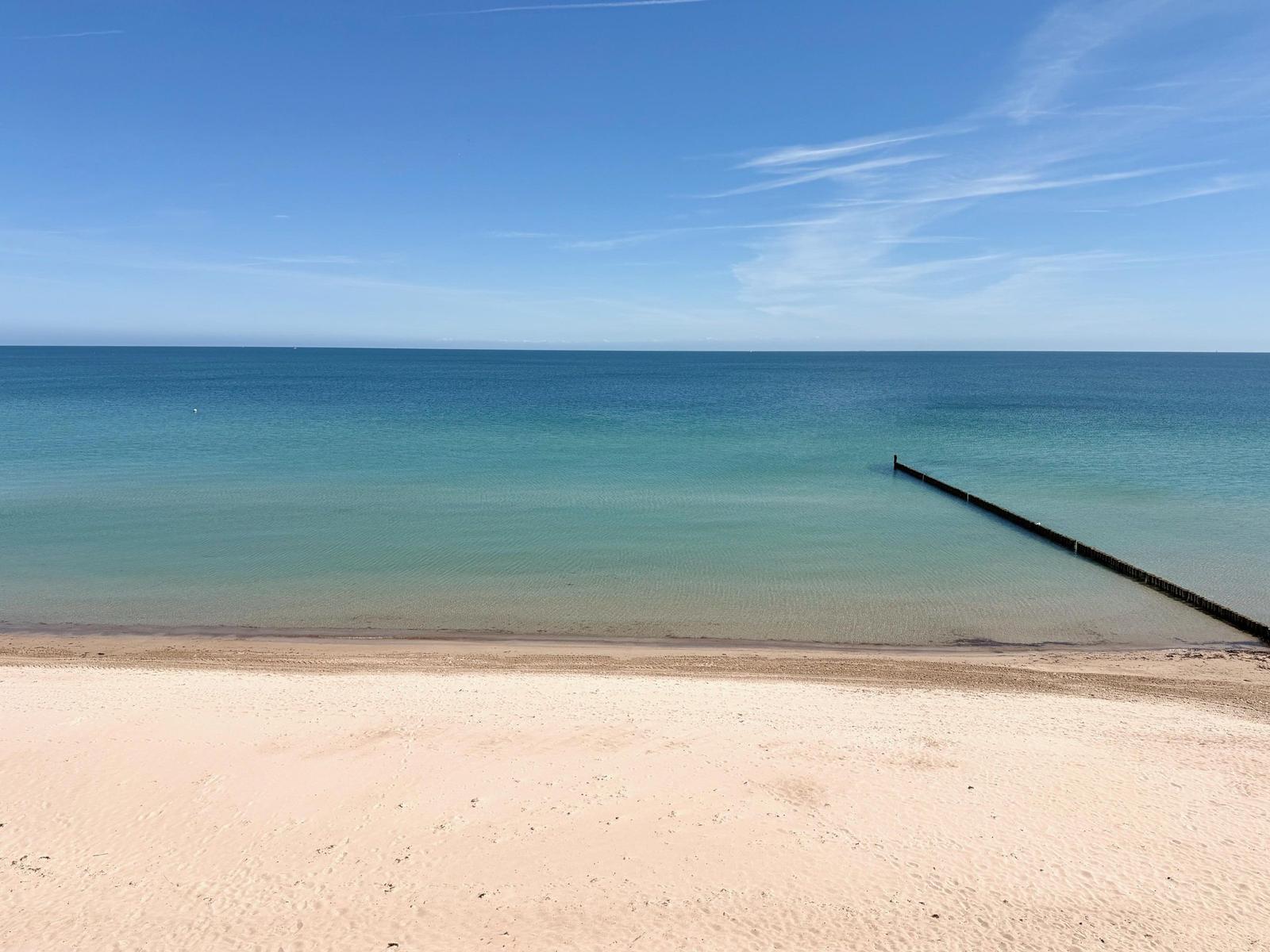 Strand mit sandigem Ufer und tiefblauem Meer unter klarer Himmel.