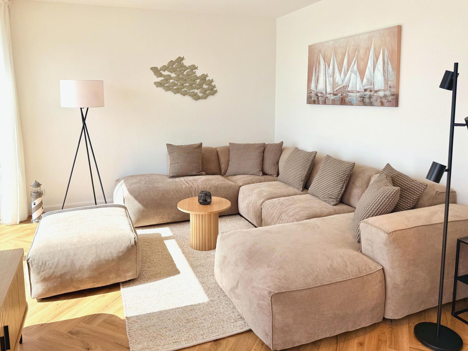 Ein Wohnzimmer mit einem großen Ecksofa, einem runden Tisch und einer Wanddekoration.