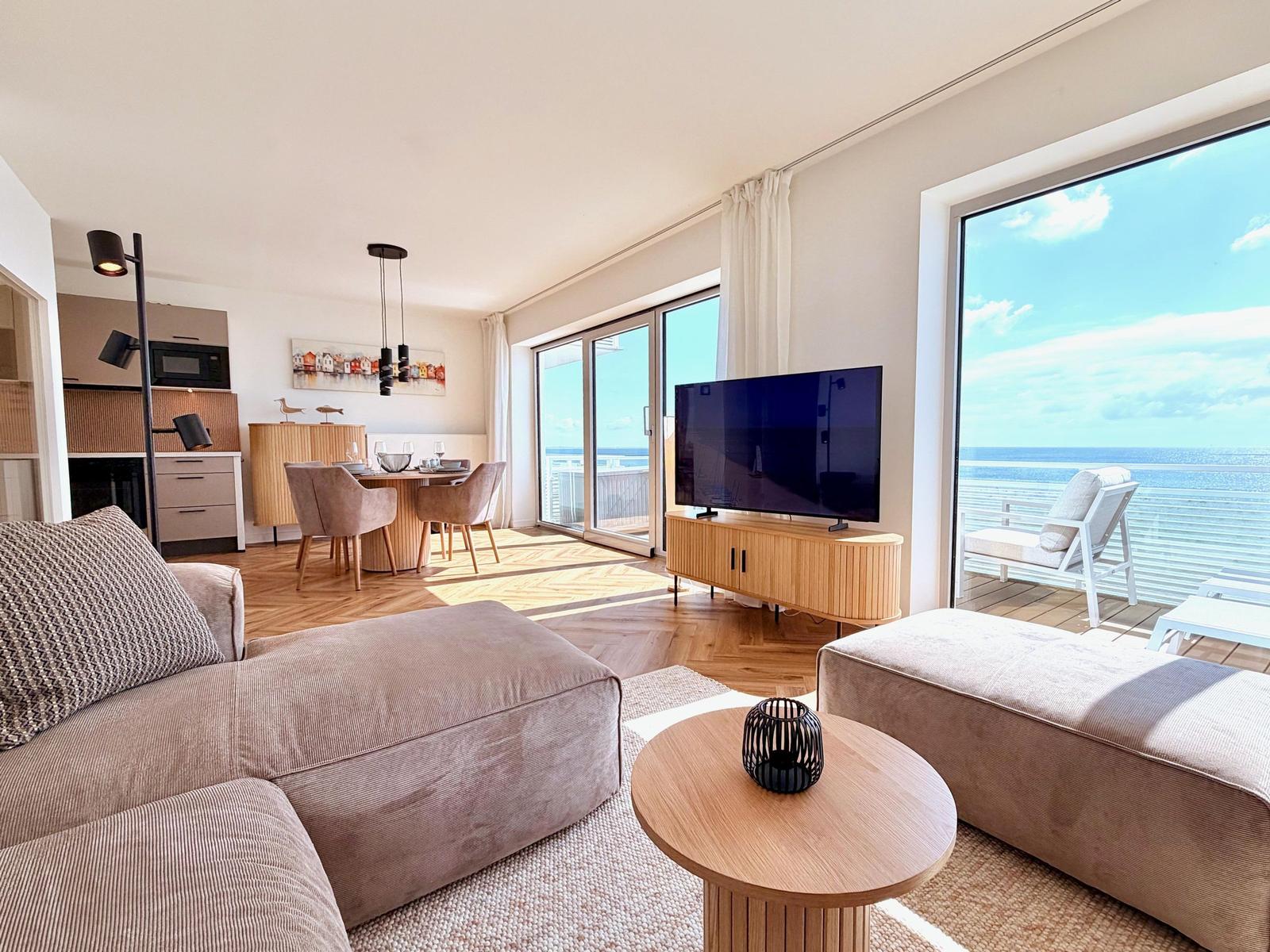 Wohn- und Essbereich mit Meerblick. Holzmöbel, Fernseher und Terrasse.