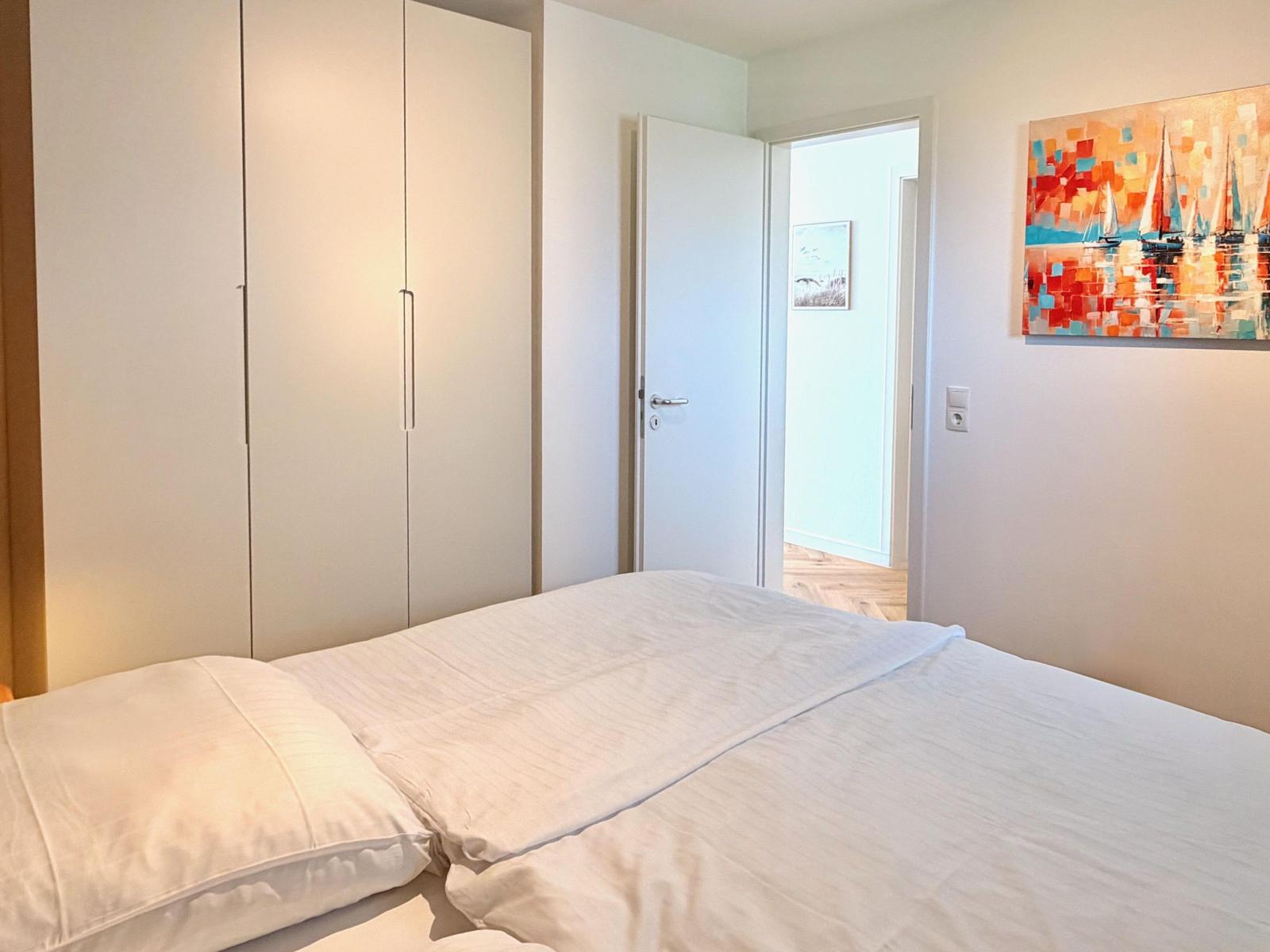Schlafzimmer mit Bett, Kleiderschrank und Wandbild mit Segelbooten.