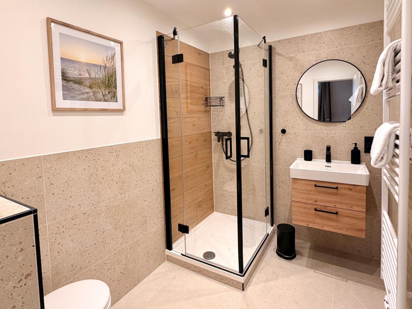 Badezimmer mit Dusche, Waschbecken und Toilette. Holz- und Steinoptik.