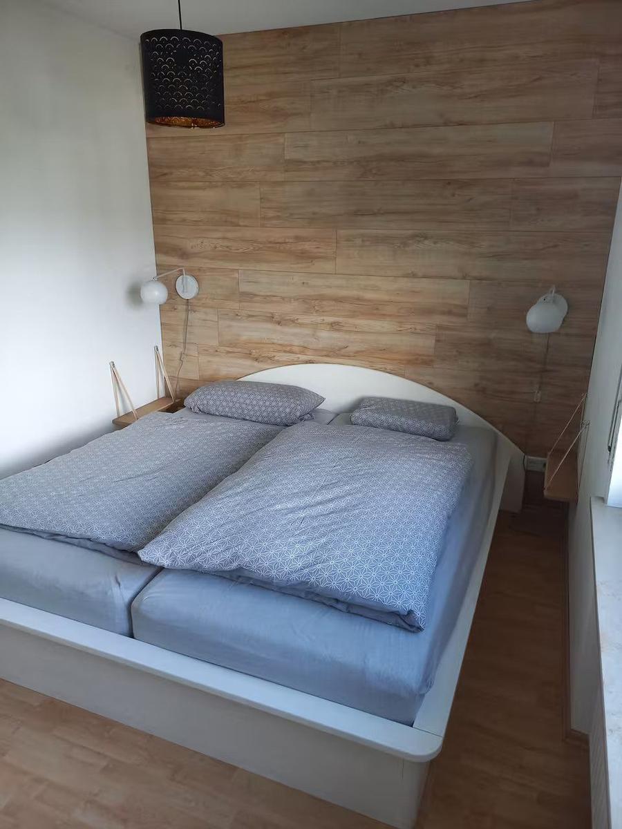 Schlafzimmer mit Doppelbett, Holzwand und Nachttischlampen.