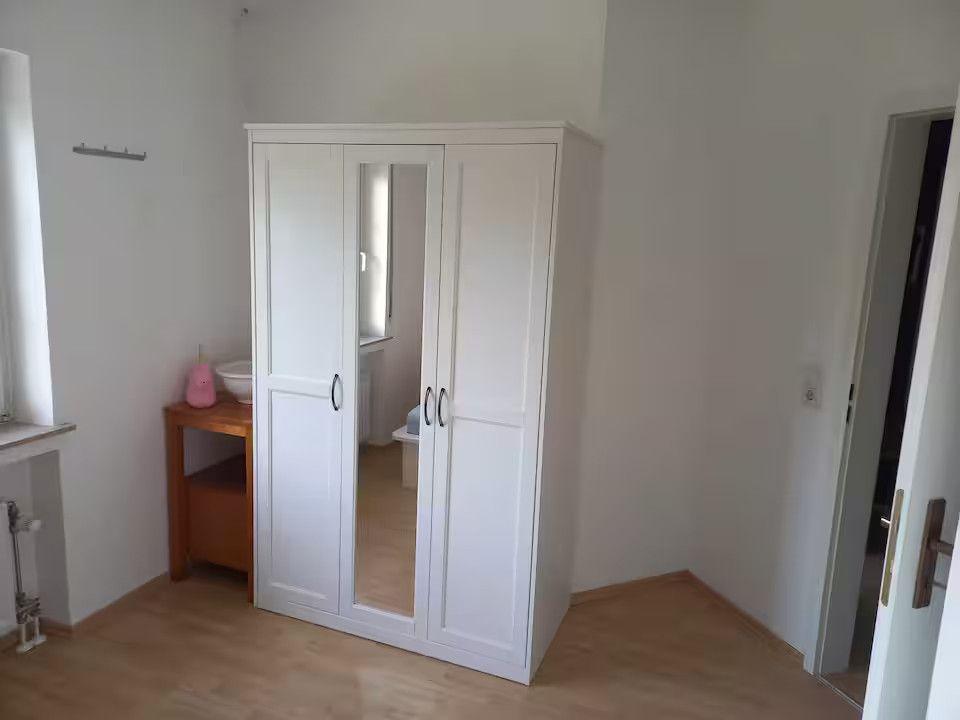 Schlafzimmer mit weißem Kleiderschrank und Holzboden. Neben dem Schrank steht ein kleiner Holztisch.