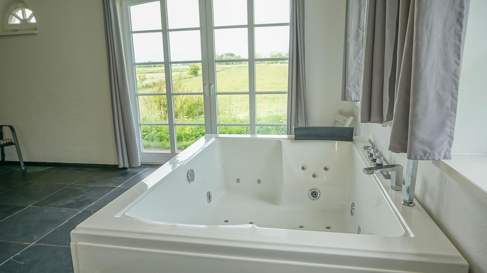 Whirlpool-Bad mit Blick auf grünes Feld durch große Fenster.