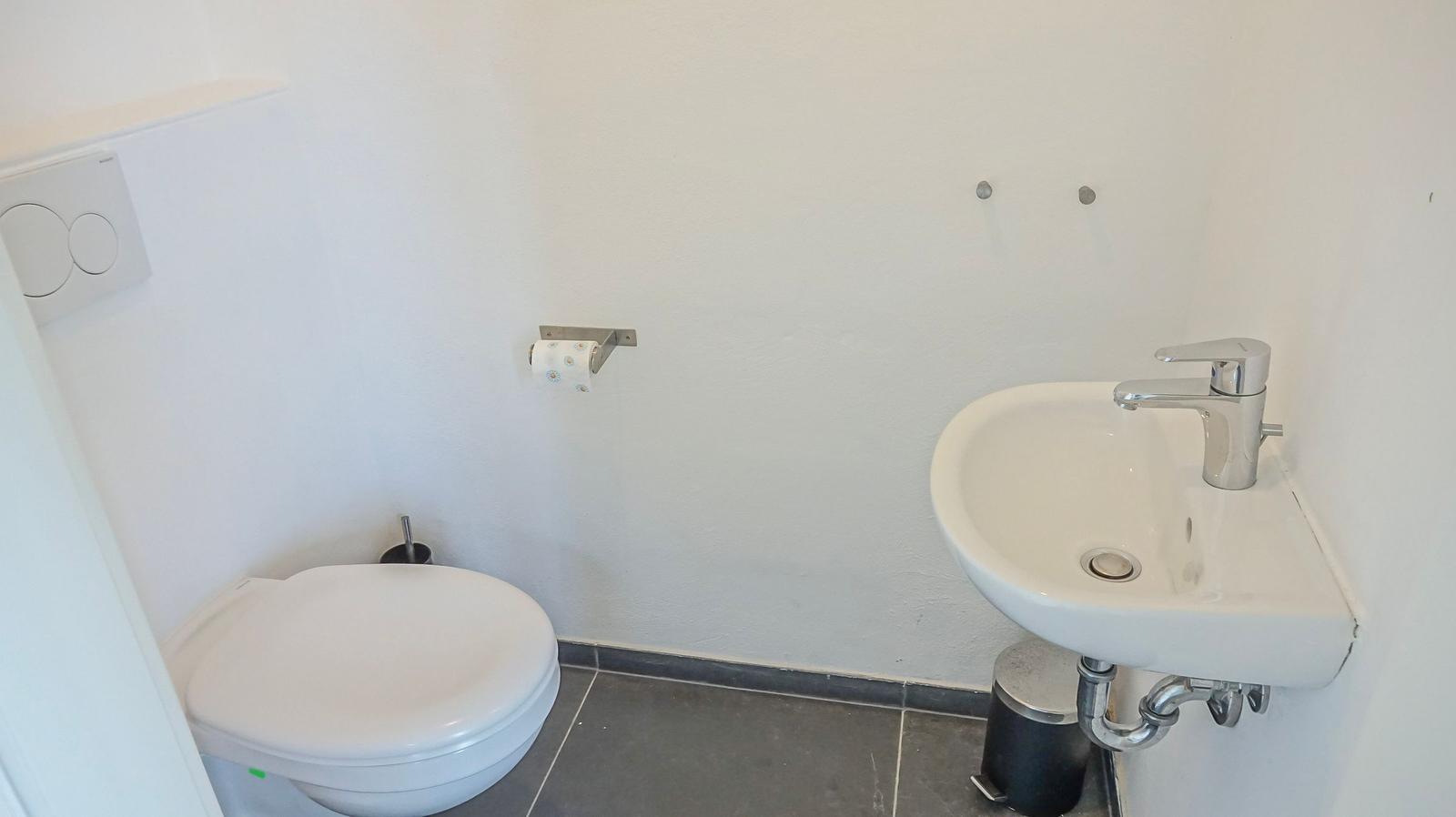 Badezimmer mit Toilette, Waschbecken und Toilettenpapierhalter.