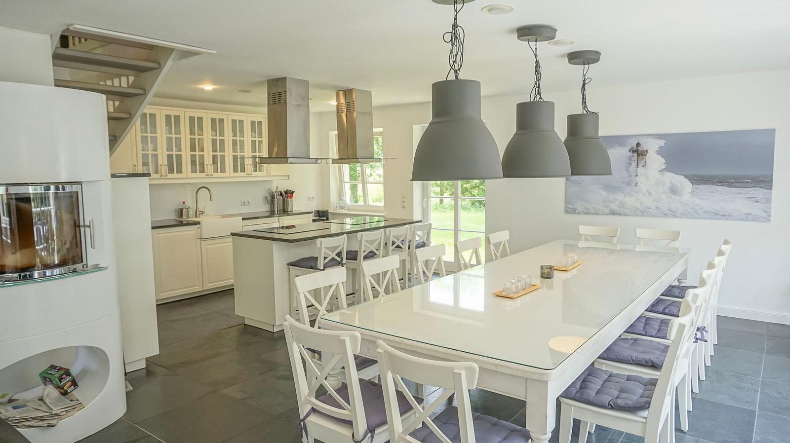 Küche und Esszimmer mit langem Tisch, weißen Stühlen und grauen Hängelampen.