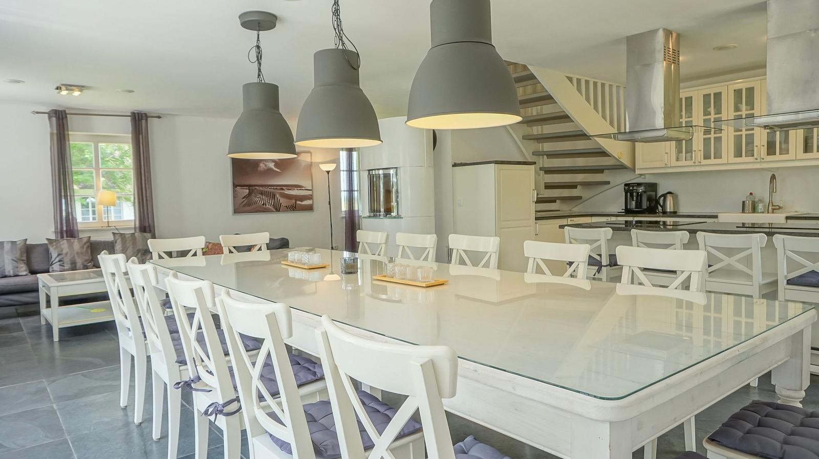 Großer Essbereich mit Glas-Tisch und weißen Stühlen. Küche und Wohnzimmer im Hintergrund.