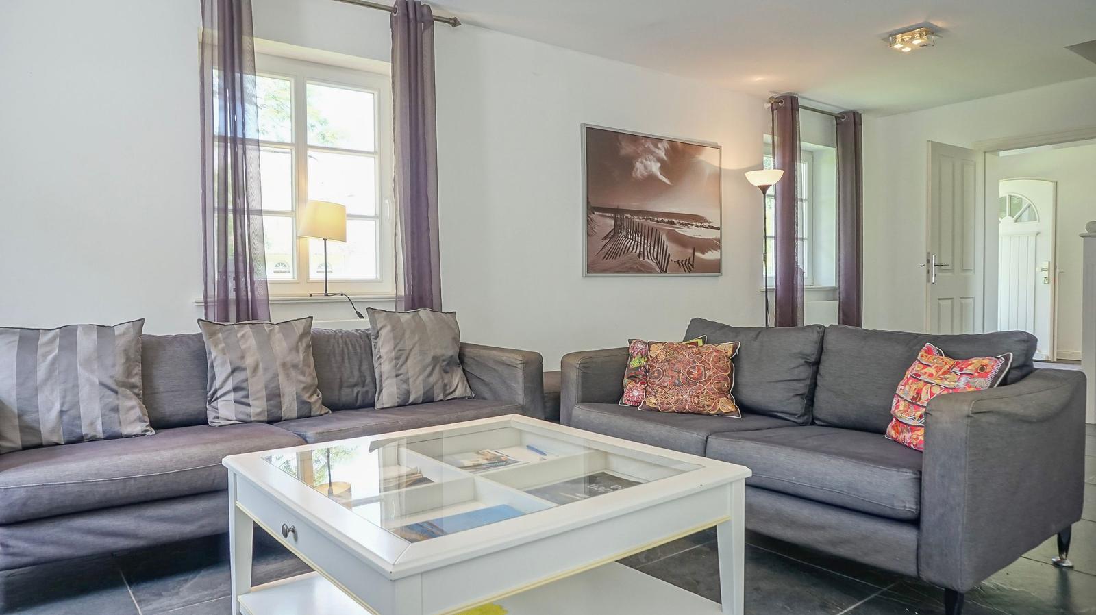 Wohnzimmer mit zwei grauen Sofas, Glas-Tisch und Wandbild.
