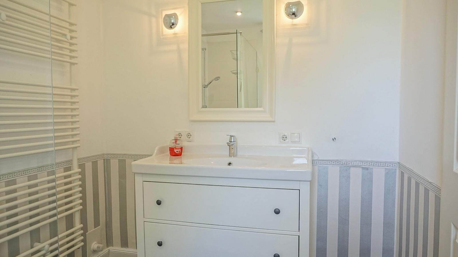 Bad mit Waschbecken, Spiegel und Dusche. Wandverkleidung mit Streifenmuster.