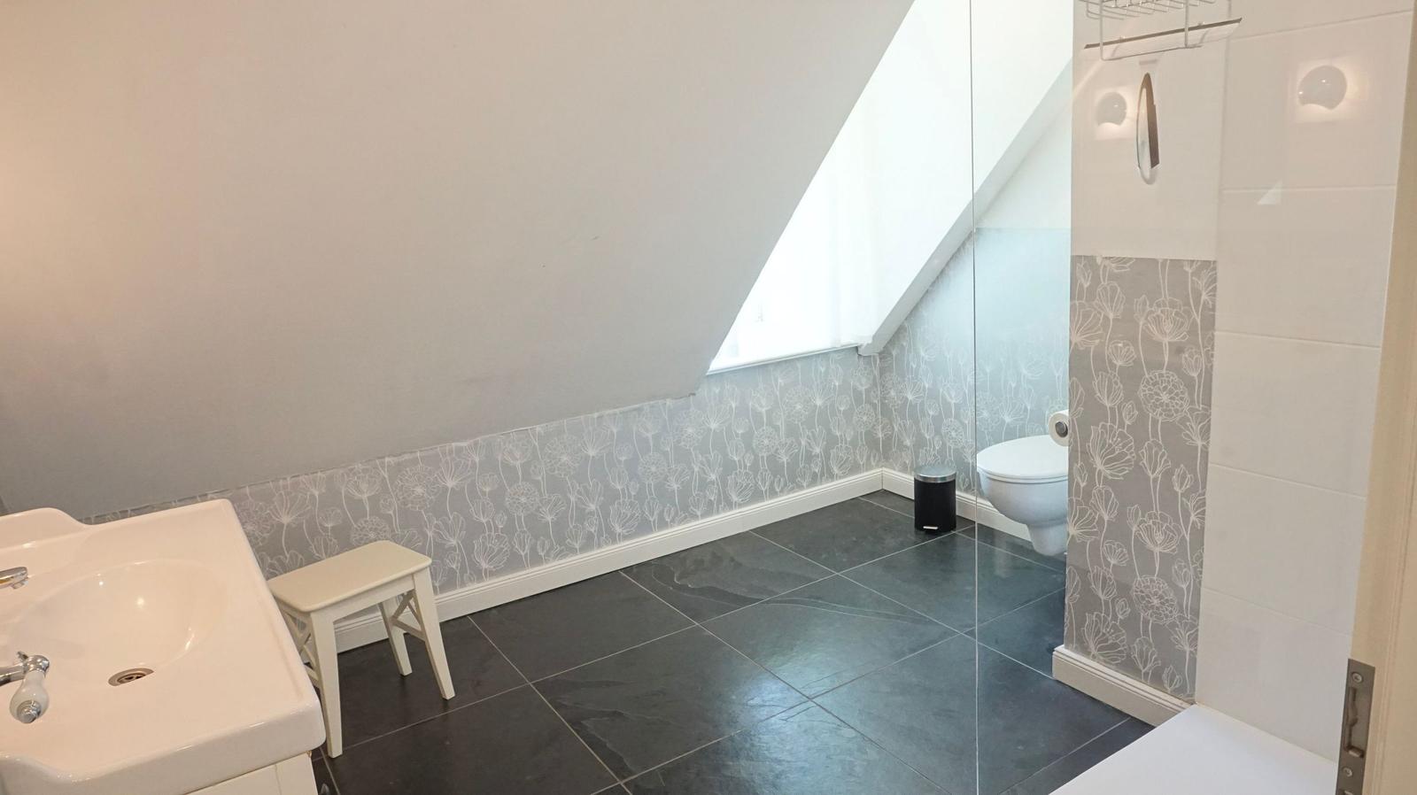 Badezimmer mit Dusche, Toilette und Waschbecken unter Dachschrägen.