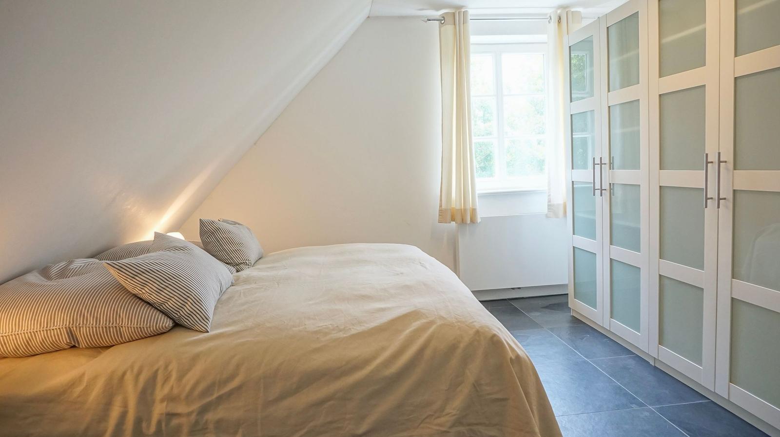 Schlafzimmer mit Dachschrägen, Bett, Fenster und Schrank.