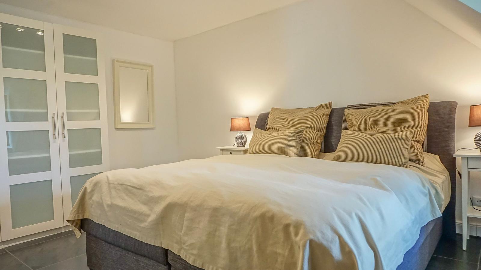 Schlafzimmer mit Bett, Nachttischen und Schrank. Wände weiß, Boden dunkel.