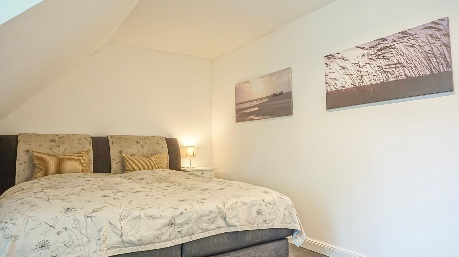 Schlafzimmer mit Doppelbett, Wandbildern und Nachttisch mit Lampe.