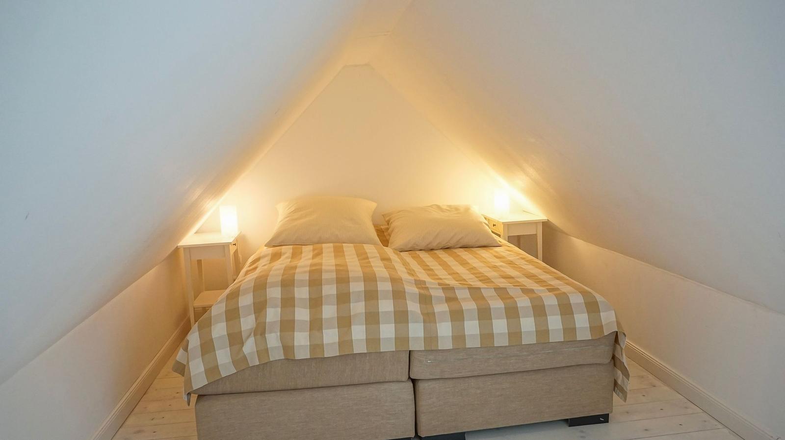 Schlafzimmer mit Doppelbett, zwei Nachttischen und schrägen Wänden.