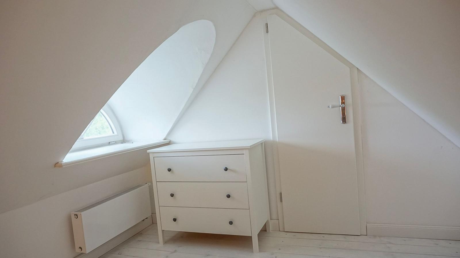 Schlafzimmer mit Dachschrägen, Fenster und weißen Möbeln.