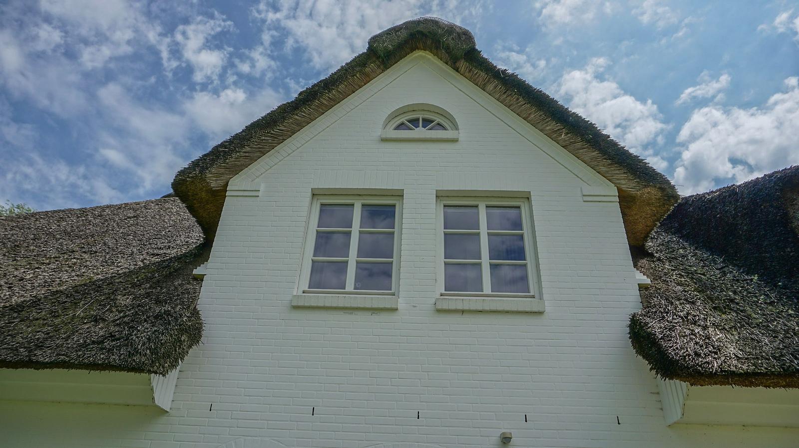 Weißes Gebäude mit strohgedecktem Dach und zwei Fenstern im Obergeschoss.