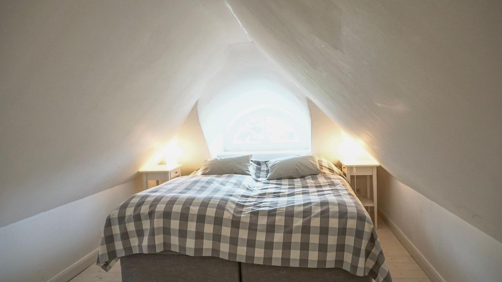 Schlafzimmer mit Dachschrägen, Bett mit kariertem Bettbezug und Fenster