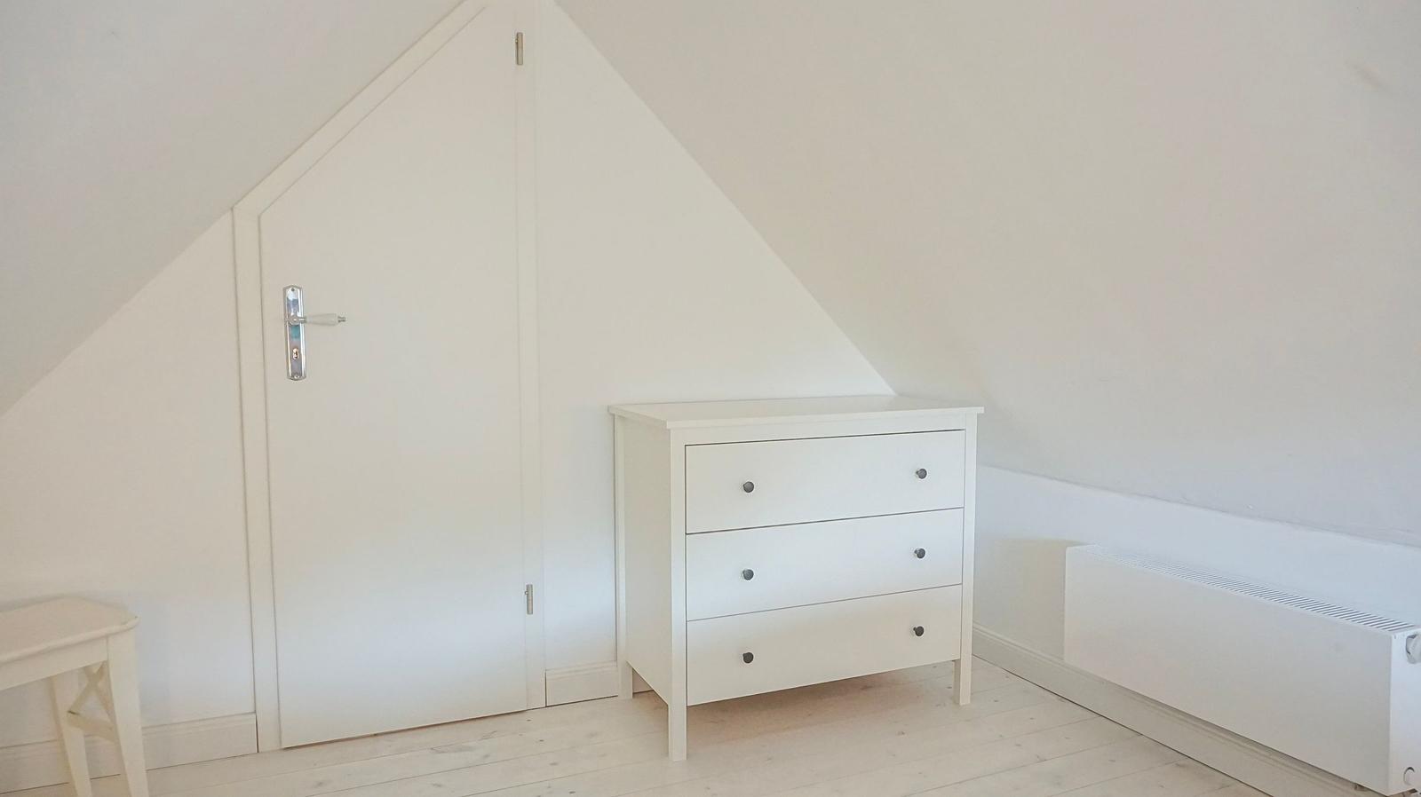 Zimmer mit weißen Wänden, Schrank und Tür unter Dachschrägen.
