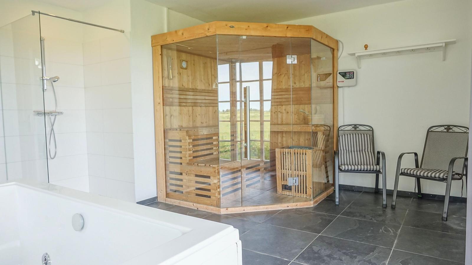 Sauna mit Glasfront und Sitzbänken, Dusche und Whirlpool im Raum.