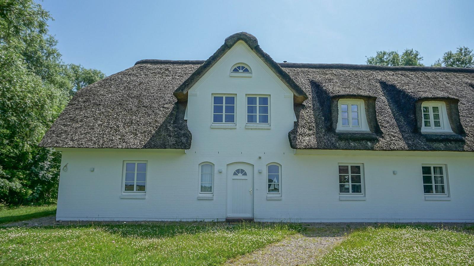 Weißes Haus mit Strohdach und mehreren Fenstern im Freien.