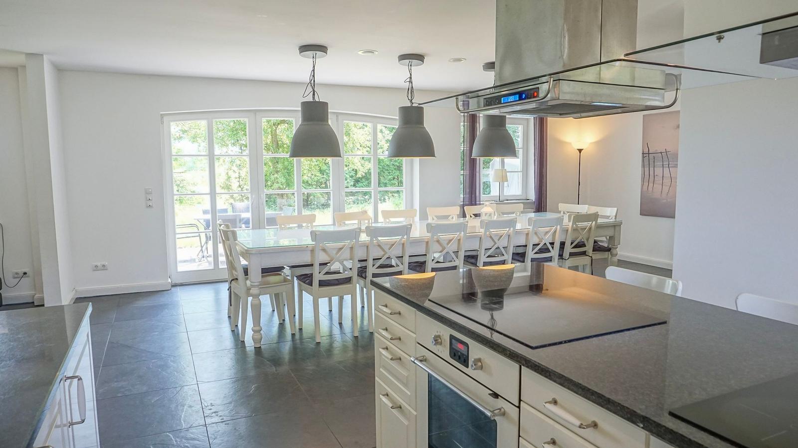 Küche mit Essbereich, Glas-Tisch, weißen Stühlen und großem Fenster zur Außenterrasse.