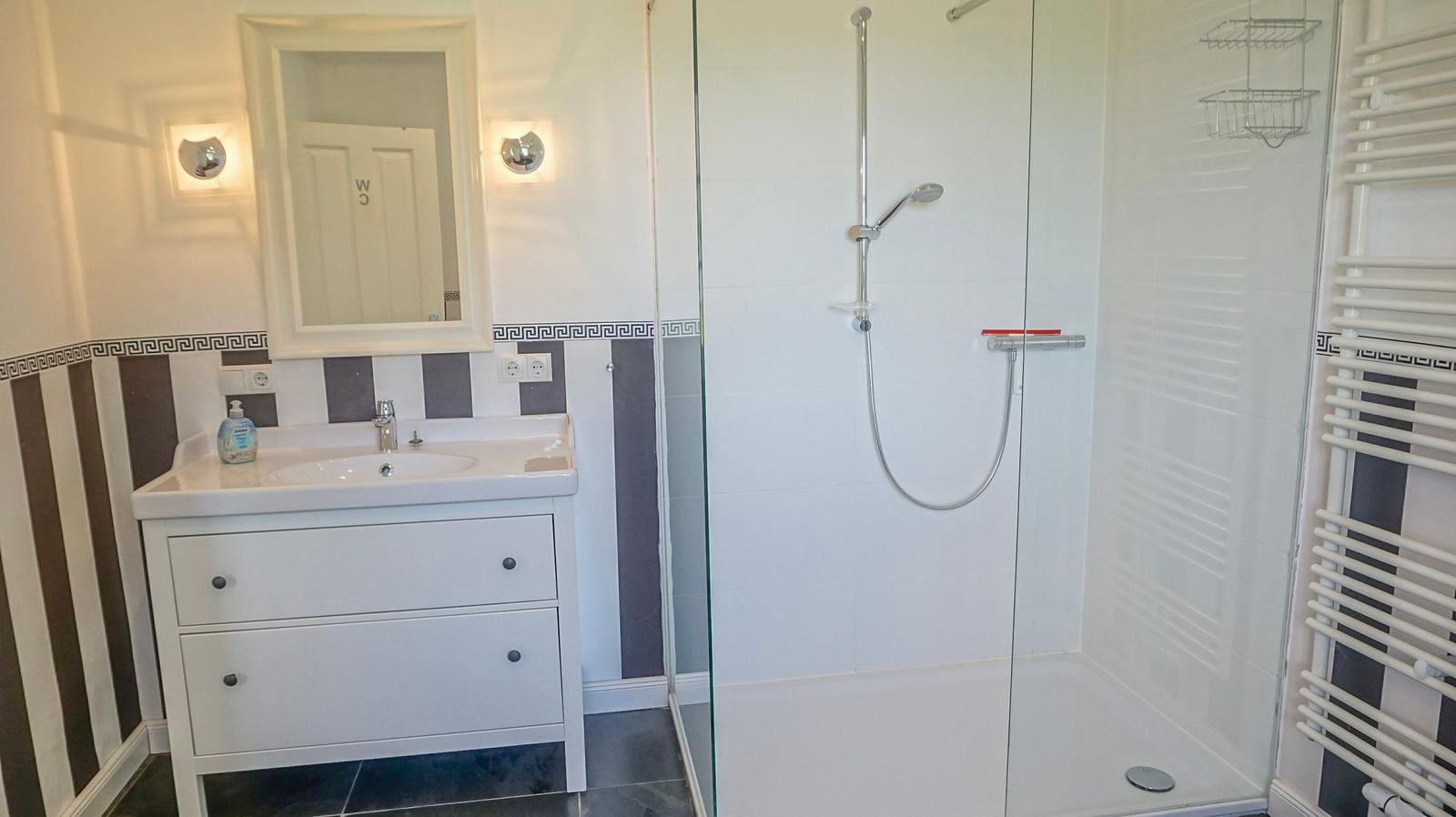 Badezimmer mit Dusche, Waschbecken und Heizkörper